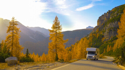 White recreational vehicle drives up empty mountain road on a sunny fall day