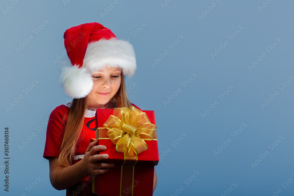 a surprised baby girl in a red Santa hat holds a Christmas gift in her hand.