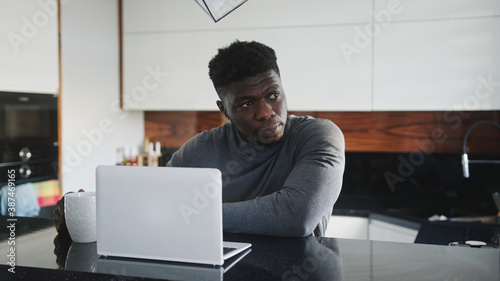 Foto young african american black man working on laptop in his appartment stretching and looking through the window