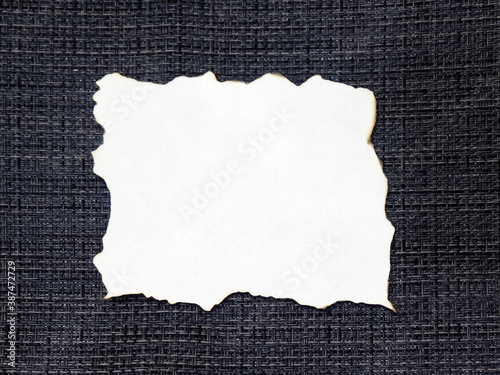 A burnt sheet of white paper on a textured gray fabric surface. Blank for design, space for text.
