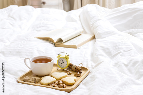 Good Morning Wishes Concept. Breakfast in bed. Beautiful composition on a wooden tray: tea with cookies, nuts. Book on the blanket is the theme of a lazy, comfortable time at home. 9:00 am.