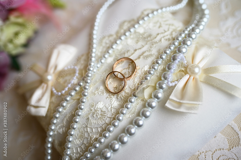 Wedding rings on a white pillow with pearls.