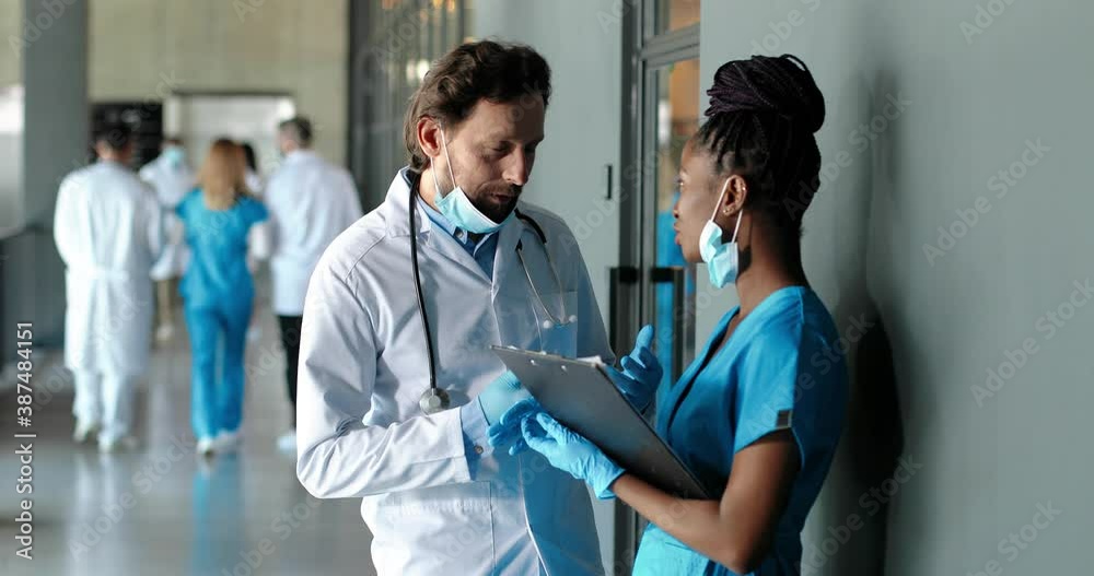 Mixed-races male and female doctors standing in hospital, talking and consulting. Professionals man and woman, physicians discussing work. Multi ethnic docs. Caucasian medic and African American nurse Mixed-races male and female doctors standing in hospital, talking and consulting. Professionals man and woman, physicians discussing work. Multi ethnic docs. Caucasian medic and African American nurse