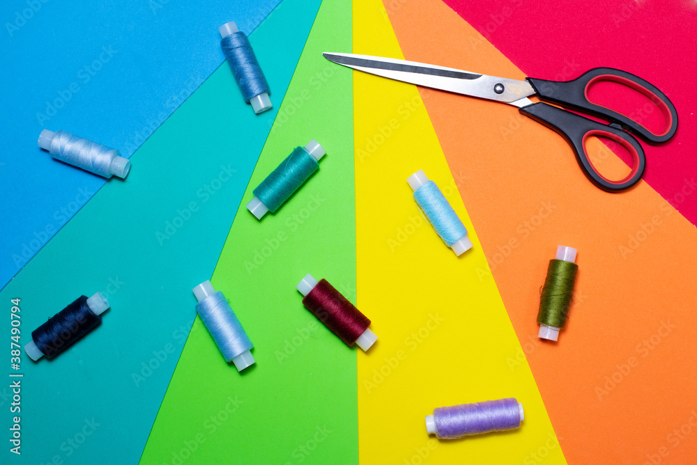 Sewing equipment. Multicolored threads and scissors on a bright background.
