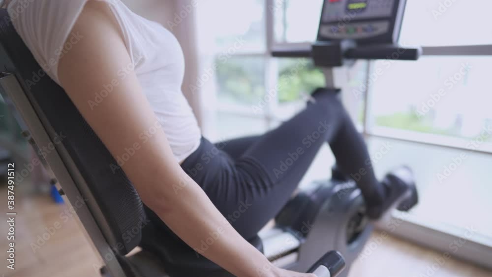 Active young woman doing cycling exercise at gym next to window. cardio fat burning training on exercise bike, fitness weight loss program, morning work out, window daylight sunny, close up shot Active young woman doing cycling exercise at gym next to window. cardio fat burning training on exercise bike, fitness weight loss program, morning work out, window daylight sunny, close up shot