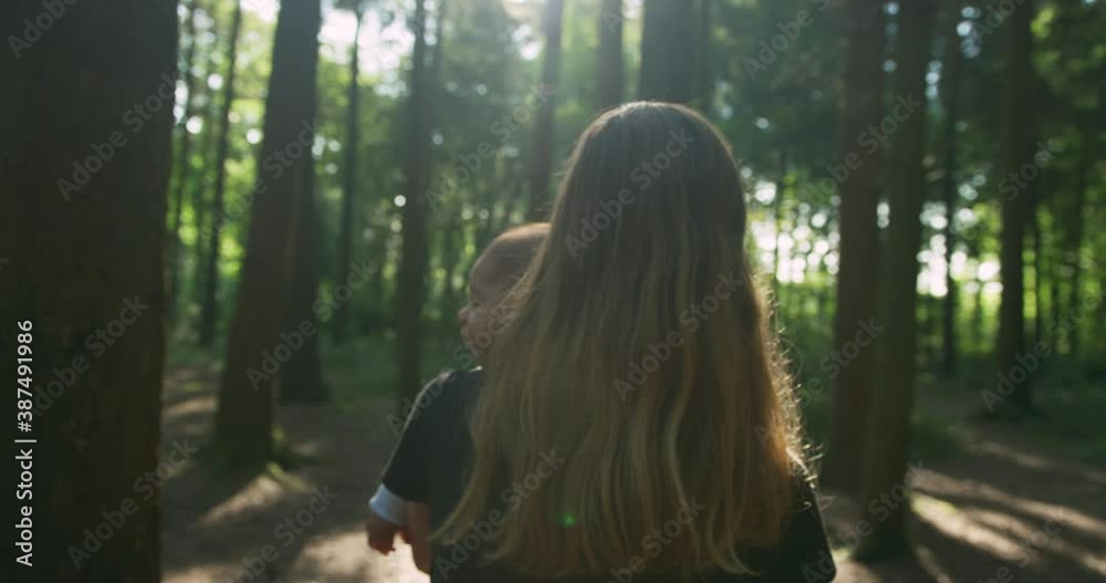 A young mother is walking and carrying her baby through a forest on a sunny summer day A young mother is walking and carrying her baby through a forest on a sunny summer day
