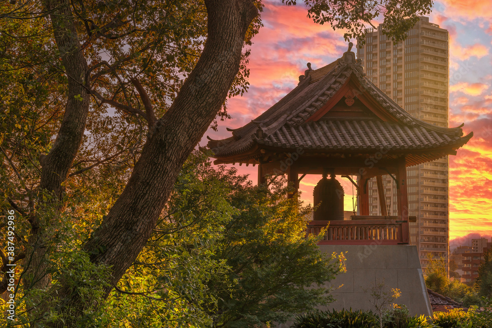 Sunset on the Shōrō bell at the foot of Daibutsu Mount in Ueno Park known as Time Bell of Kaneiji Temple made famous by Matsuo Basho with skyscraper in background.