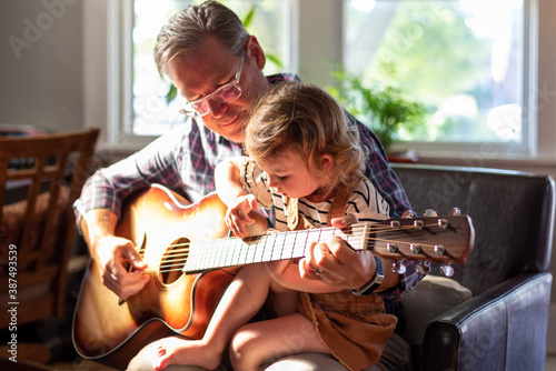 Grandpa and granddaughter playing guitar in the living room in natural sunlight
