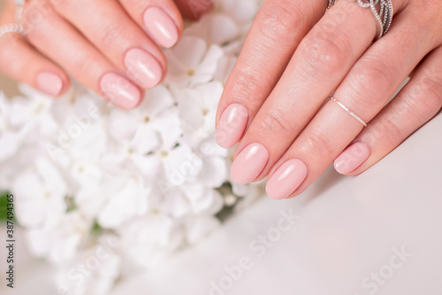 Beautiful female hands with wedding manicure nails, nude gel polish and white flowers