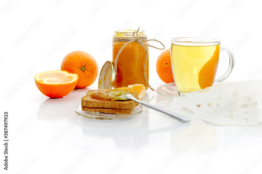Orange jam in a jar, tea in a cup, oranges and rusks on a wooden table close-up