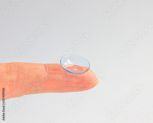 Contact lens on human finger on grey background. Selective focus. Close up