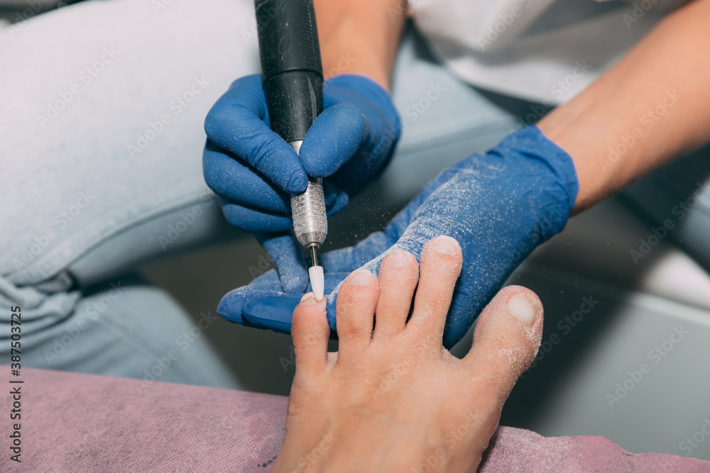 Pedicure process in salon. Foot care treatment and nail. The process of professional pedicures. Master in blue gloves makes pedicure with manicure machine. Concept of beauty care and health.