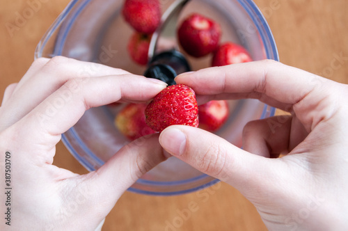 Hands put a strawberry in a blender, top view