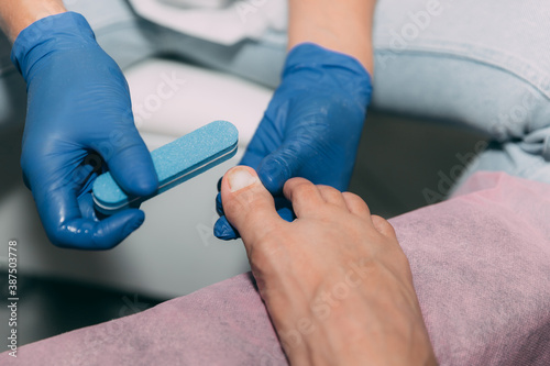 Close-up pedicure process in salon. Foot care treatment and nail. Sanding nails with a nail file. Master in blue gloves makes pedicure with manicure machine. Concept of beauty care and health.