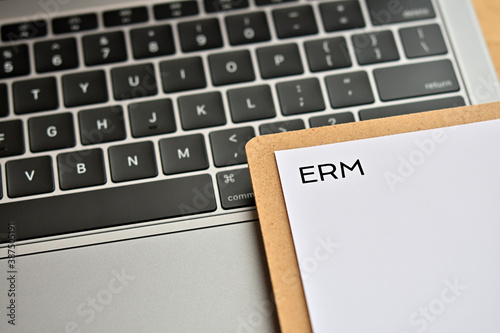 A piece of paper with the word "ERM" written on it sits on the keyboard. That's an acronym for "Enterprise Risk Management". Closeup. 