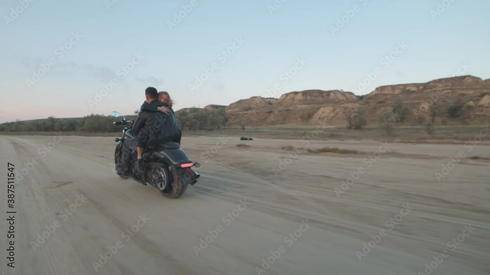 Guy with a girl on a motorcycle in the desert. Couple riding on vintage motorcycle and having a good time at sunset on a dry salt lake. Slow motion shot