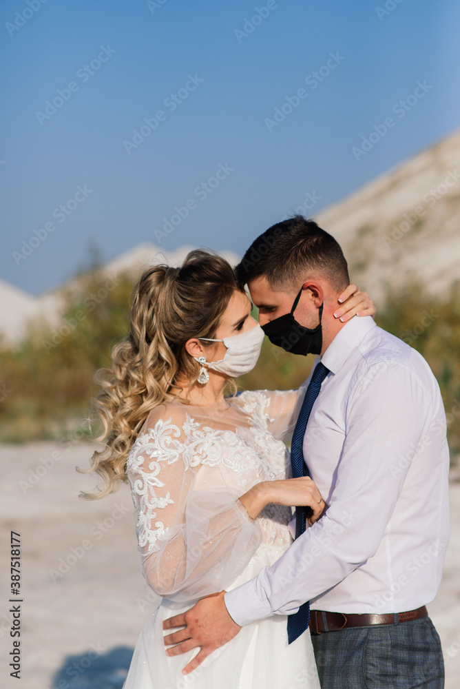 Young loving couple in medical masks in park during quarantine on wedding day. Young loving couple in medical masks in park during quarantine on wedding day.