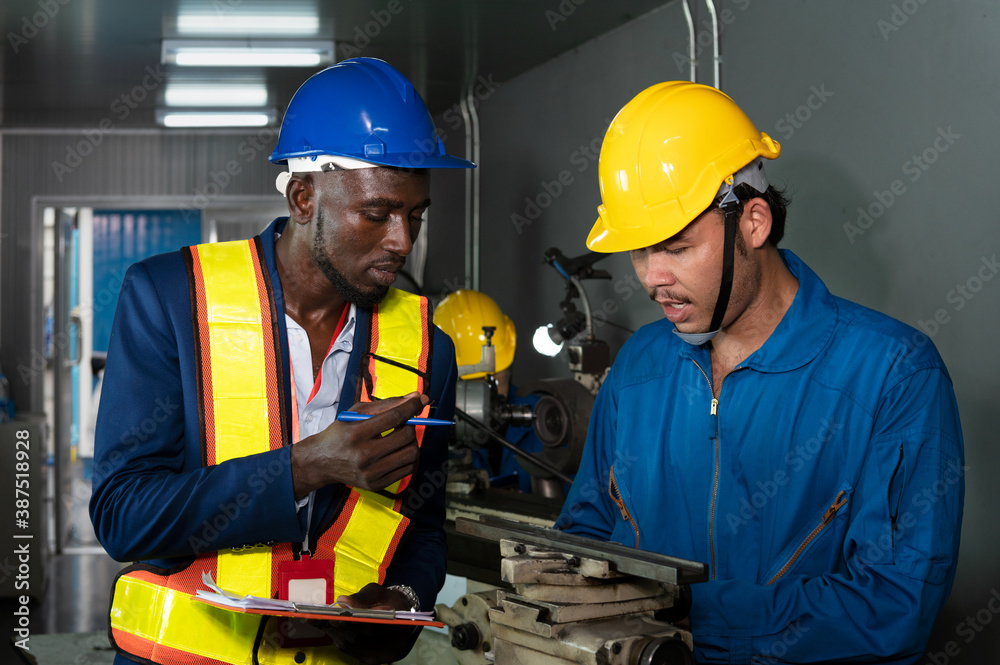Male technician inspector discusses with male factory mechanic expert in front of a repair machine in factory maintenance office with protective glasses, gloves and helmet in factory uniform Male technician inspector discusses with male factory mechanic expert in front of a repair machine in factory maintenance office with protective glasses, gloves and helmet in factory uniform