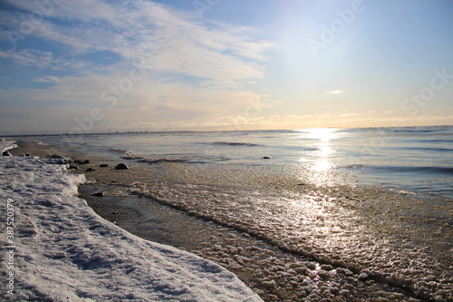 Fototapeta Naklejka Na Ścianę i Meble -  Snow lies on the sand by the sea. Clouds in the sky and waves on the water