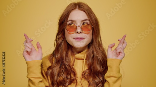 Redhead girl crossing fingers for luck in studio. Cute woman hoping indoors