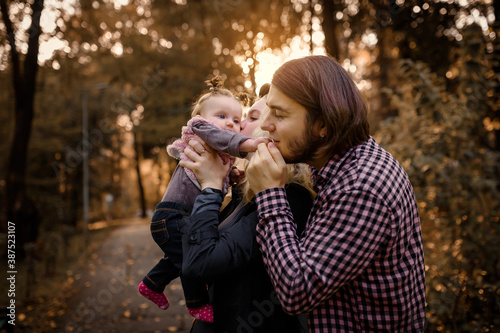 Young father and mother are kissing their 6 month old baby child girl in the park during the fall walk.