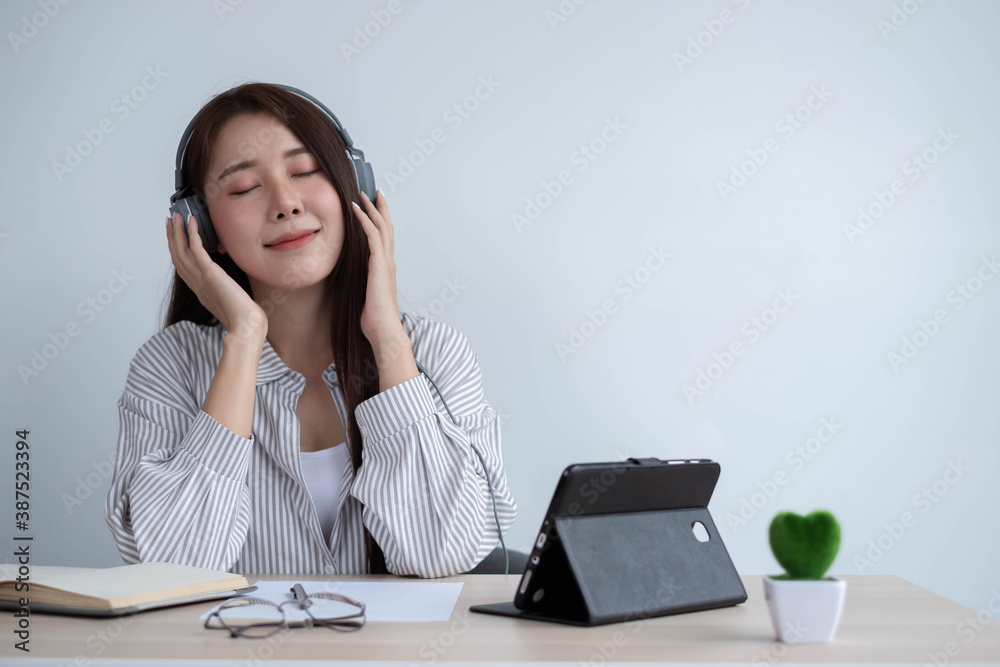 An Asian woman is resting by wearing headphones to listen to music to relieve the stress of working hard in her room. An Asian woman is resting by wearing headphones to listen to music to relieve the stress of working hard in her room.