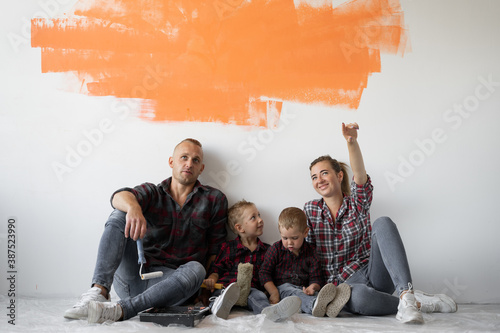 family of four people sit on the floor near the wall mom raised her index finger up.