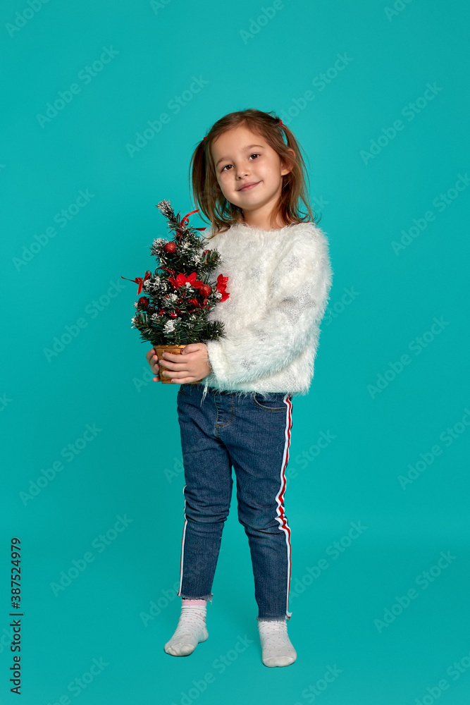 Merry Christmas and happy holidays. Cute little baby girl holding a Christmas tree. Christmas holiday concept. Merry Christmas and happy holidays. Cute little baby girl holding a Christmas tree. Christmas holiday concept.