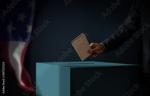 Election Day in United States of America Concept. Person Dropping a Ballot Card into the Vote Box. USA Flag hanging on the Wall. Dark Cinematic Tone photo