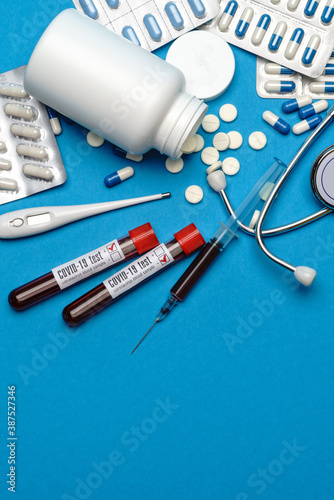 Stethoscope, syringe, thermometer, blood test tube and can of pills on blue background top view with copy space