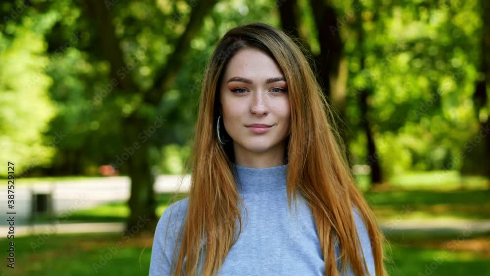 Portrait of attractive modern woman with red hair looking at camera at sunny park Portrait of attractive modern woman with red hair looking at camera at sunny park