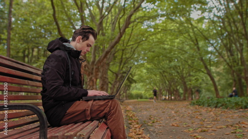 Young man sitting with a laptop in the park .serious teenage, guy, young man, student working on laptop in the park. Remote work and learning concept