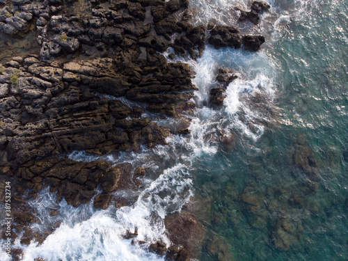 Aerial top down image of ocean sea waves splashing with white foam against rocks, rocky cliff, coast, island Crete, Greece. Sea patterns, background wallpaper.