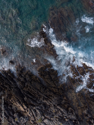 Aerial top down image of ocean sea waves splashing with white foam against rocks  rocky cliff  coast  island Crete  Greece. Sea patterns  background wallpaper.
