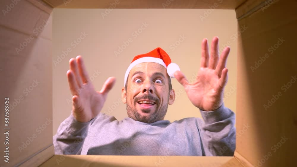 Happy man wearing xmas hat unpacking christmas gift seen from inside box