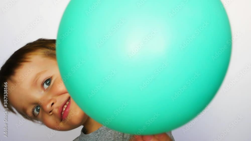 A little boy holds a turquoise balloon close to the camera and looks out behind it A little boy holds a turquoise balloon close to the camera and looks out behind it