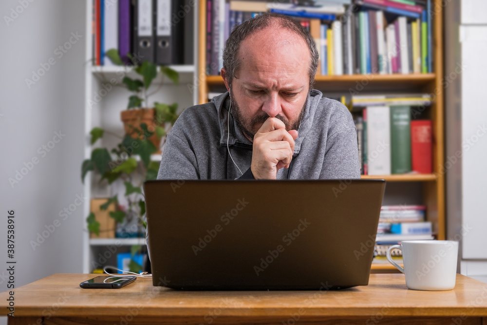 Man working online from home office on computer laptop behind vintage desk, concentrated, with earphones, listening online meeting Man working online from home office on computer laptop behind vintage desk, concentrated, with earphones, listening online meeting