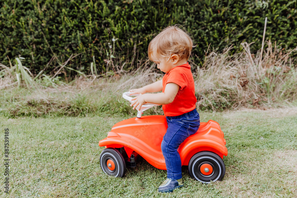 Baby girl riding toy car in garden Baby girl riding toy car in garden