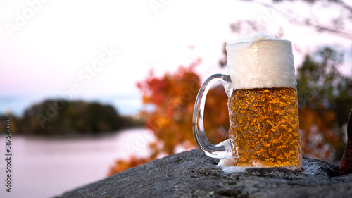 A cold lager beer sits on the rocks of the suburban archipelago in Stockholm, Sweden, on a cold and crisp autumn evening. Leafs are changing colors in the background.
