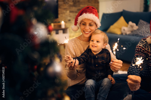 Happy mother and her small son having fun with sparklers on Christmas eve.