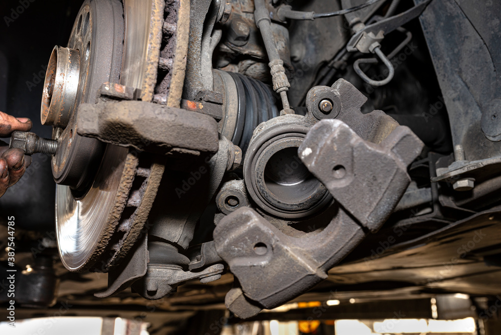 Disassembled front brake caliper on the car, which is on the car jack in the workshop, close-up of the brake caliper.