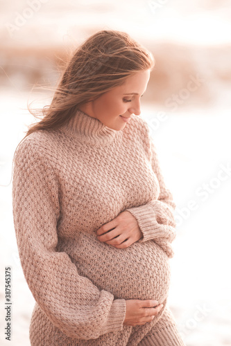 Pregnant woman wearing knitted comfy sweater holding tummy over sea outdoors close up. Motherhood. Maternity. 20s. Healthcare. Healthy lifestyle. photo