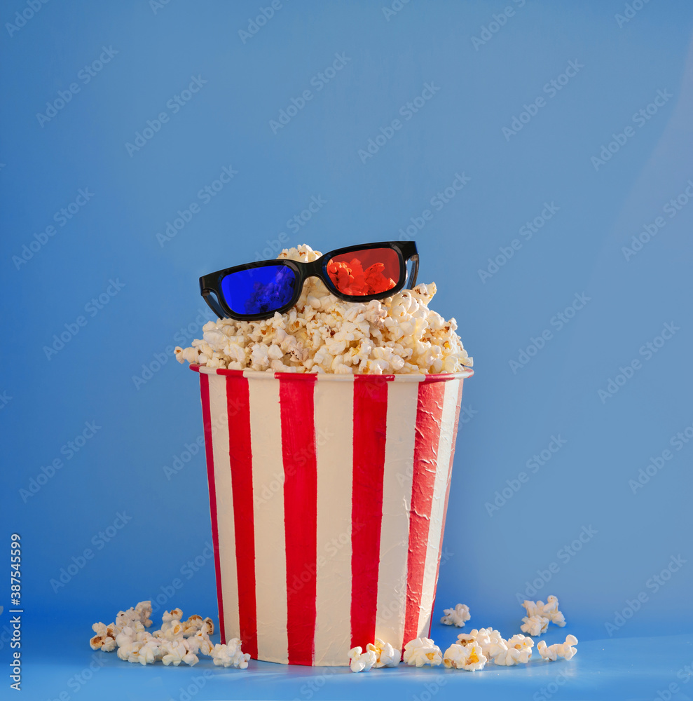 A bucket full of popcorn on a blue background and 3D glasses