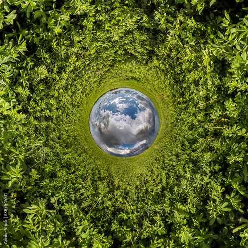 Inversion of blue tiny planet transformation of spherical panorama 360 degrees. Spherical abstract aerial view on green grass field with awesome beautiful clouds. Curvature of space.