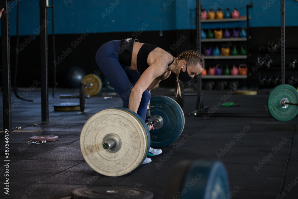 Chica con mascarilla en un gimnasio realizando Cross training, clean and jerk Chica con mascarilla en un gimnasio realizando Cross training, clean and jerk