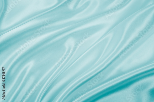 Photography of beautiful wavy turquoise silk satin luxury cloth fabric, abstract background design.