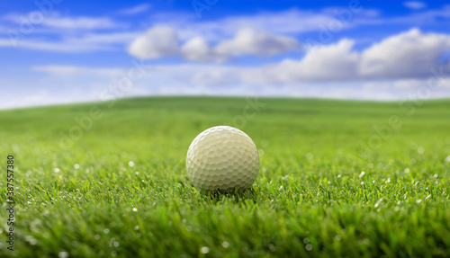 Golfball on green grass golf course, blue cloudy sky background