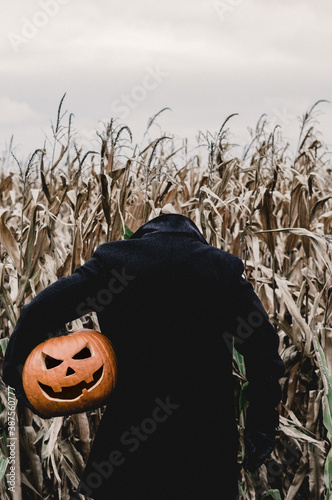Scary Halloween man is holding his pumpkin head by his side 