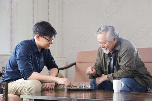 Senior Asian man playing chess with his son in the living room for elder and family concept