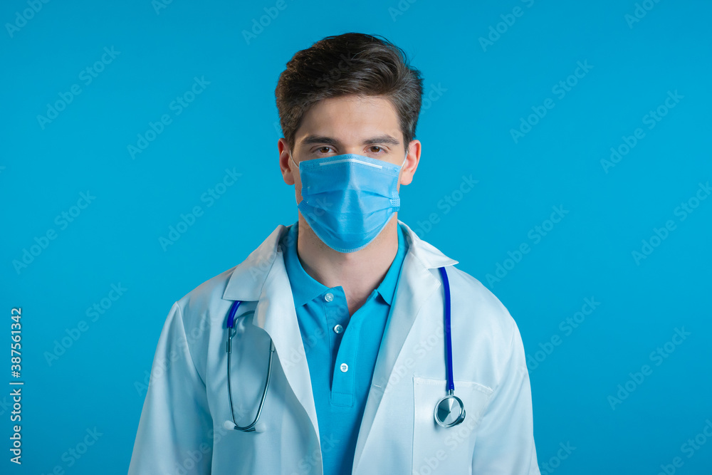 Portrait of serious doctor in professional medical mask and coat. Doc man isolated on blue background. Portrait of serious doctor in professional medical mask and coat. Doc man isolated on blue background.